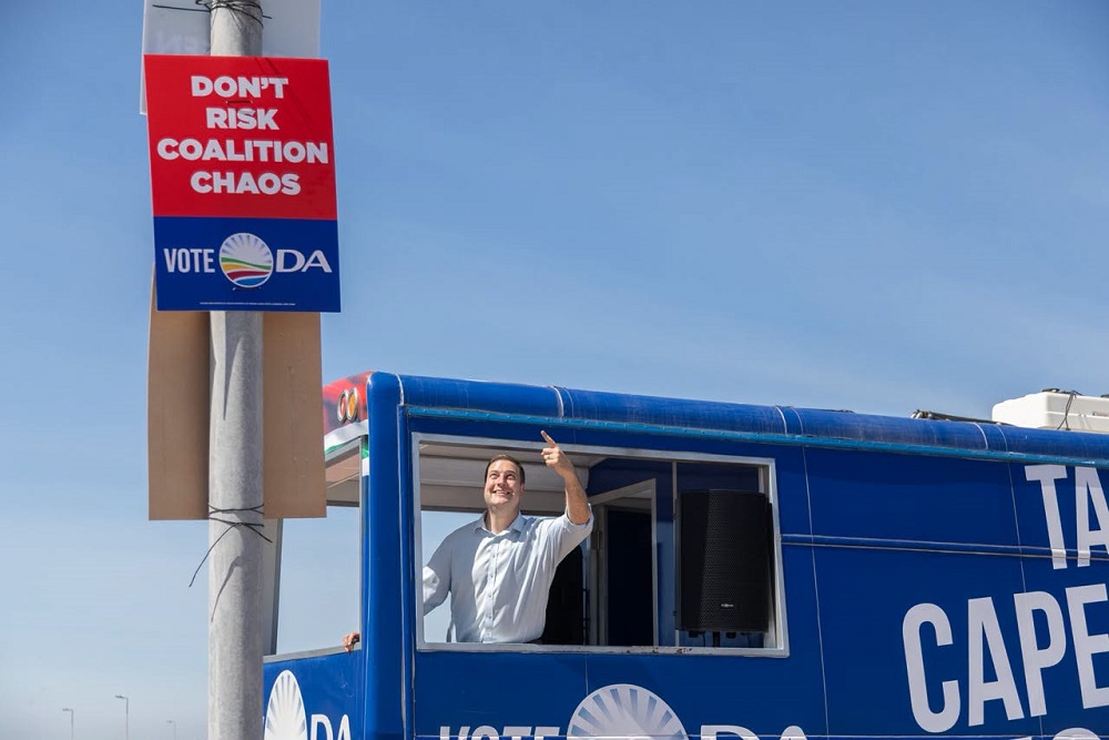 DA leader and City of Cape Town mayoral candidate Geordin Hill-Lewis points to a poster saying “Don’t risk coalition chaos” as he campaigns in Bloubergstrand in the West Coast on 27 October 2026.